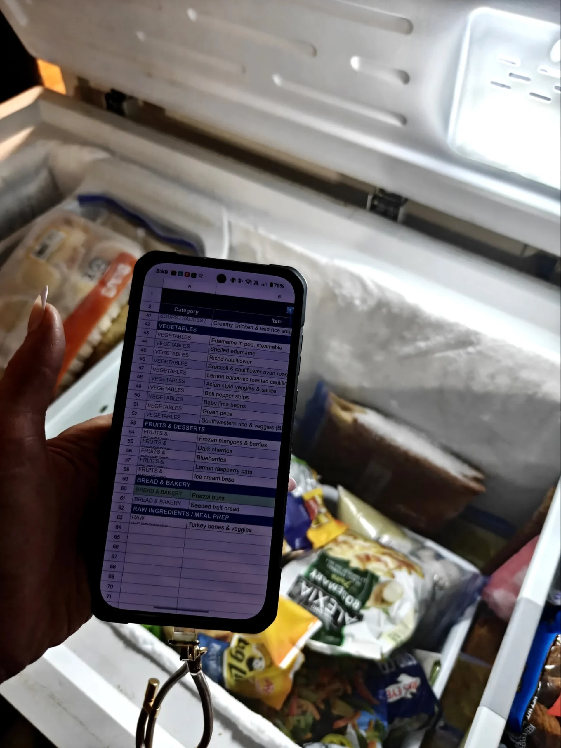 A phone screen showing a frozen food inventory organized into categories, held in front of an open freezer.